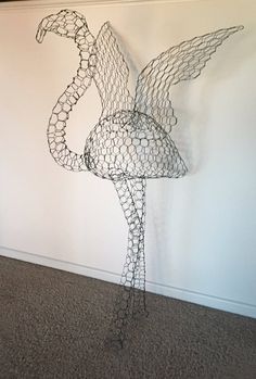 a wire sculpture of a flamingo standing in front of a wall