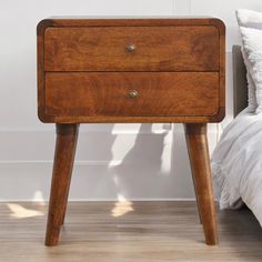 a small wooden table with two drawers on one side and a white pillow on the other