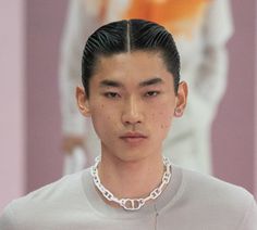 a young man with black hair wearing a necklace