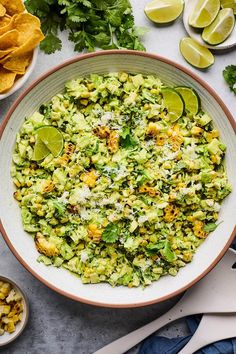 a bowl filled with guacamole, limes and tortilla chips