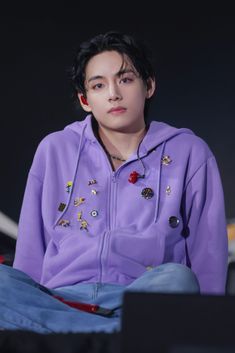 a young man sitting on top of a bed wearing a purple jacket