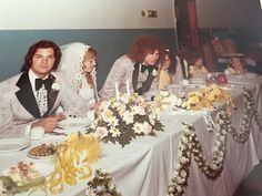 a group of people sitting at a table with plates and flowers in front of them