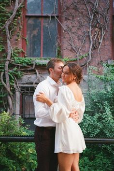 a man and woman embracing each other in front of a building with ivy covered windows