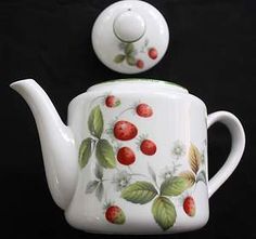 a teapot with berries painted on it and a cup next to it, both sitting side by side