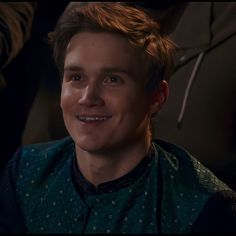 a young man smiling at the camera while wearing a green shirt and black vest with stars on it