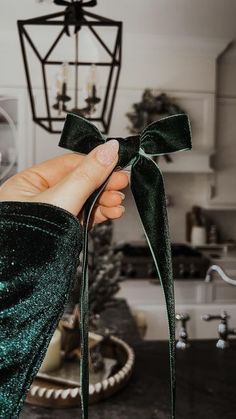 a hand holding a green bow in front of a chandelier hanging from the ceiling