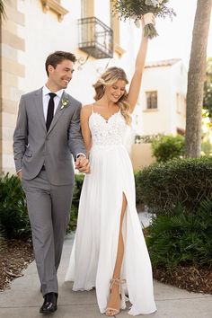 a man and woman walking down a sidewalk holding hands with each other, both dressed in grey suits