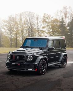 a black mercedes g63 amg is driving down the road with trees in the background