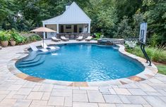 a backyard with a pool, patio and lounge chairs in the foreground is a gazebo