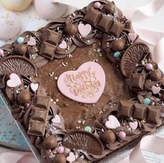 a heart shaped cake with chocolate frosting and candies on the top, surrounded by confetti