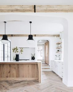 an open kitchen with white walls and wood flooring on the side, along with two black pendant lights hanging from the ceiling