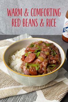 a white bowl filled with rice and red beans next to a bottle of hot sauce