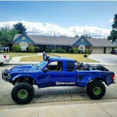 a blue pick up truck parked in front of a house with large tires on it