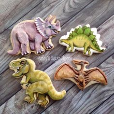 four dinosaur cookies are sitting on a wooden table