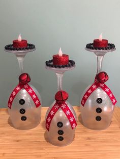 three wine glasses with candles in them sitting on a wooden table next to each other