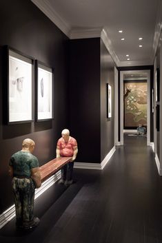 two statues are sitting on the bench in front of an art gallery with black walls and white trim