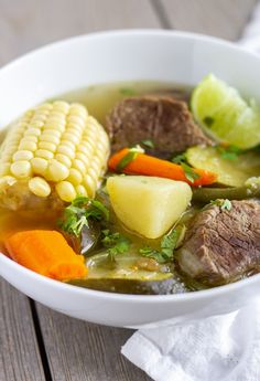 a white bowl filled with meat, vegetables and corn on top of a wooden table