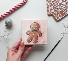 a hand is holding a small square tile with a gingerbread man on it, surrounded by christmas decorations and candy canes