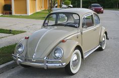 an old vw bug parked on the side of the road in front of a house