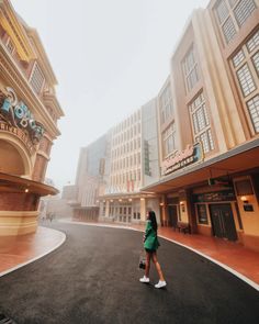 a woman walking down the middle of a street in front of some buildings and shops