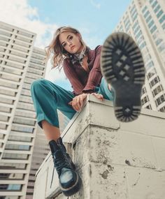 a woman sitting on top of a wall next to tall buildings with her feet up