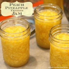 three mason jars filled with pineapple jam sitting on a table next to a pot