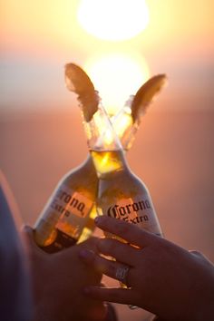 two people toasting with corona beer in front of the sun