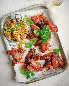 a metal tray topped with wings covered in sauce and garnish