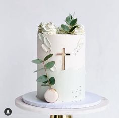 a white cake decorated with flowers and a cross on the top is sitting on a stand