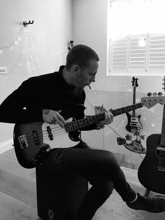 a man sitting on top of a stool while playing an electric guitar in front of him