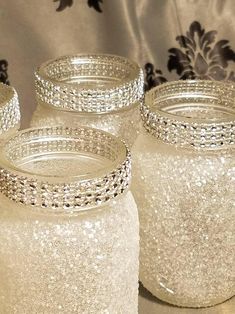 four glass jars with beaded rims are sitting on a cloth covered tablecloth