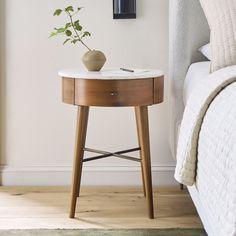 a small table with a vase on it next to a bed