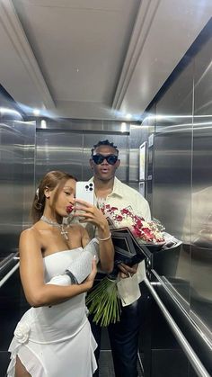 a man and woman standing in an elevator taking pictures with their cell phones while holding flowers