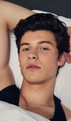 a young man laying in bed with his arm on the back of someone's head