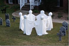 three ghost statues are standing in the grass near headstones and tombstones with white cloth draped over them