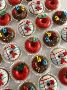 there are many decorated cupcakes in the box on the table and one has an apple