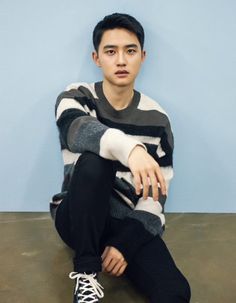 a young man sitting on the ground with his legs crossed wearing black pants and a striped sweater