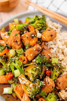 a plate with rice, broccoli and chicken on it next to chopsticks