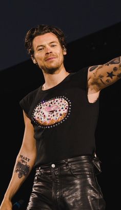 a man in black shirt and leather pants holding his arm out to the side with one hand