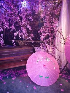 two pink umbrellas sitting on the ground in front of a tree with purple flowers