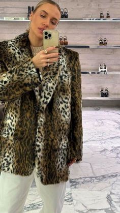 a woman taking a selfie with her cell phone while wearing a leopard print coat