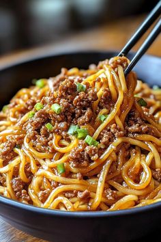 a black bowl filled with noodles and meat on top of a wooden table next to chopsticks