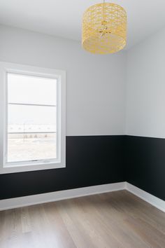 an empty room with black and white walls, wood floors and a yellow chandelier