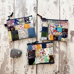 three small zippered pouches are sitting on a white wooden surface, one has a gray hat and the other is made out of patchwork fabric