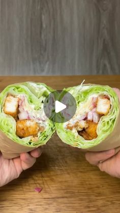 two hands holding up some food on top of a wooden table