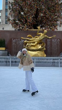 a woman is standing in front of a fountain with a large golden statue behind her