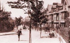 an old black and white photo of people walking down the street in front of houses