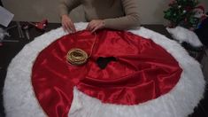 a woman is making a santa hat on top of a christmas tree skirt with scissors