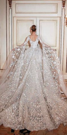 a woman in a wedding dress standing next to a wall with a large veil on it's back