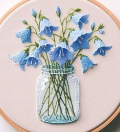 blue flowers are in a mason jar on a white surface, and the embroidery is stitched